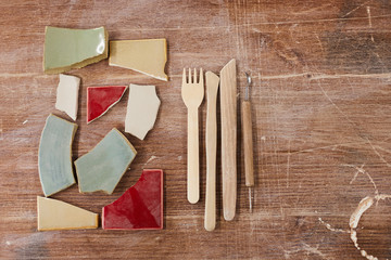 High angle view of various wooden tools for ceramic design and colorful ceramic parts on scratched...