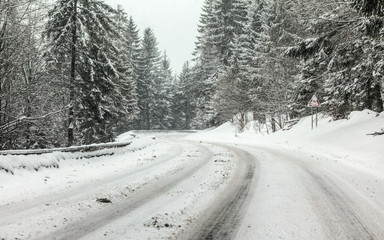 Curve on forest road covered with snow, more falling, dangerous driving conditions