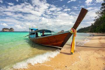 Thailand typical Long-tail boat on clear azure green sea, sky with small clouds above, golden beach on right, Koh Kradan island in Krabi region