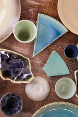 High angle view of ceramic dishware and shards of broken plates in pastel colors placed on old scratched table