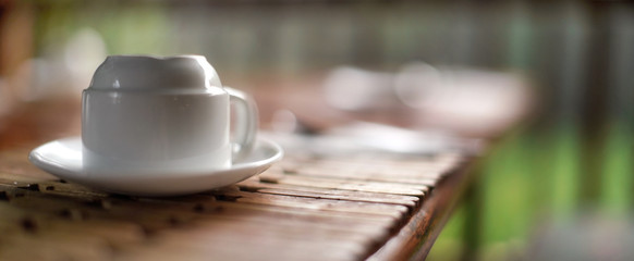 Empty white porcelain cup, upside down, on wooden table, blurred green background. Very shallow depth of field photo - only edges and few wood boards in focus, space for text right