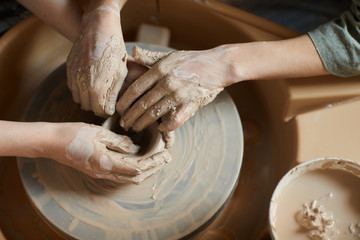 Fototapeta na wymiar High angle view of unrecognizable women with hands smeared with clay using pottery wheel while moulding vase together