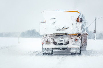 Plow gritter truck on snow covered road during snowstorm, view from car behind