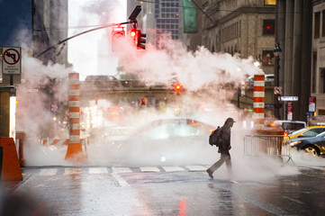 A black male is crossing the 42nd street in Manhattan while steam coming out from from the manholes. 42nd Street is a major crosstown street in Manhattan, New York, USA.