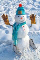 Cute little snowman outdoor. The snowman is wearing a fur hat and scarf. Snow man outdoor. Snowman isolated on snow background. Snowman in a scarf and hat.