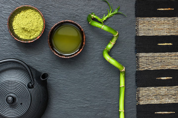 Set of matcha - powder in  bowl,  green tea in cup  and  dark ceramic teapot