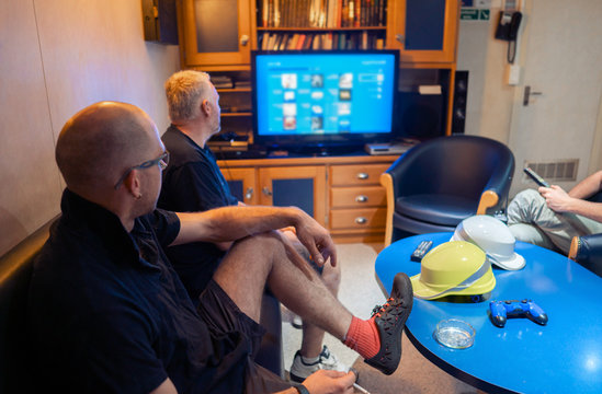 Happy team of ship officers watch TV onboard of vessel. TV, recreation and internet at sea