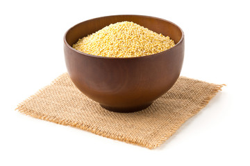 Pile of golden millet, a gluten free grain seed, in wooden bowl on burlap fabric over white