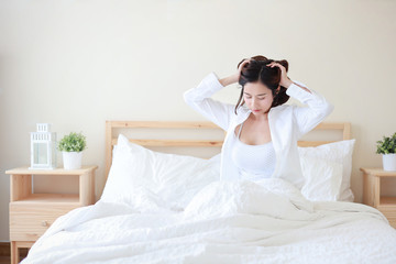 Fototapeta na wymiar Cheerful and sexy asian young woman wearing white shirt wake up in the morning and sitting and stretching on bed in bedroom with relaxation and happy face