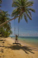 female tourist on a swing hanging from a palm tree on the beach in summer