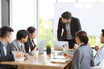 caucasian lecturer giving public presentation with company business graph result on white board in meeting room and multiethnic business people are paying attention (training or seminar concept)