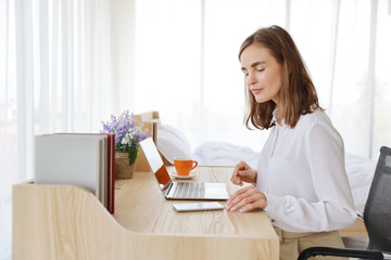 beautiful caucasian girl drinking a cup of coffee or tea in the morning with laptop computer and cell phone on wood table in bedroom