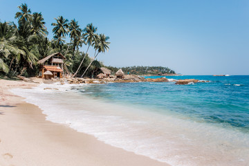 White sand & blue water in Tangalle. Goyambokka beach with palm & house on the shore, in the southern province of Sri Lanka. Majestic bay in Indian Ocean. Waves breaking on the most beautiful stones.