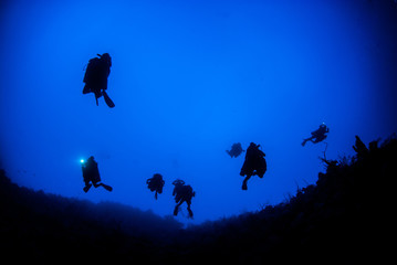 A silhouette shot of scuba divers using rebreather equipment are captured here just about to descend to depths of up to 300 feet. The shot was taken at the top of the wall in the Cayman Islands