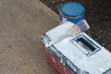 still life of tool kit paintbrush and can of blue paint outside on a sidewalk beside a bed of mulch preparing to paint house trim with of copy space