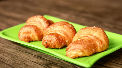 Croissants on green plate. Wood background. 