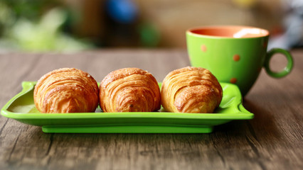 Croissants on green plate and a cup of drink. Wood background. 