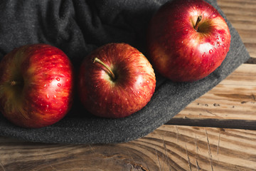 three fresh red apples on wooden table and blue fabric with a lot of contrast