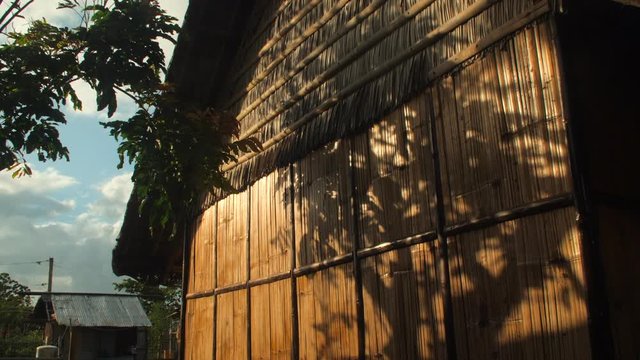 Wind blowing through tree casting a shadow on a bamboo hut in a local village during sunset in slow motion, glowing orange light, Caramoan Islands Philippines