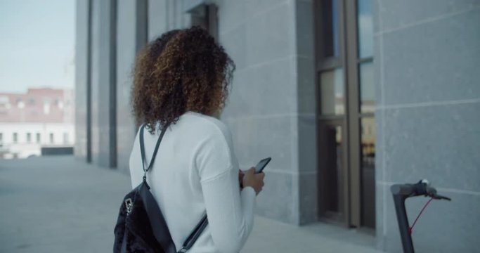 Attractive African American black female uses her phone to unlock and rent an electric city shared scooter. 4K UHD 60 FPS SLOW MOTION