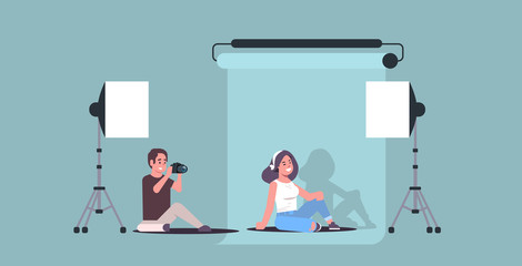 professional photographer using camera man shooting beautiful sexy woman model sitting posing in modern photo studio interior horizontal full length flat