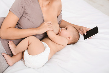 Millennial mother using smartphone during breastfeeding baby