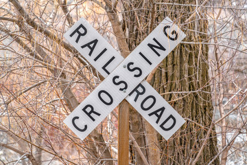 White and black Railroad Crossing sign with leafless trees in the background - Powered by Adobe