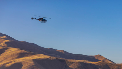 Helicopter flying over an immense mountain with clear blue sky background