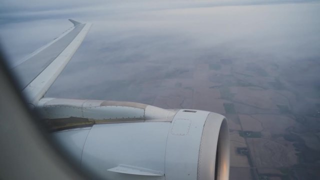 Flying in a plane overlooking the clouds and ground with the side engine in frame.