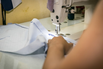 seamstress on a sewing machine makes a shirt in the sewing workshop. close-up partial view of seamstress working.