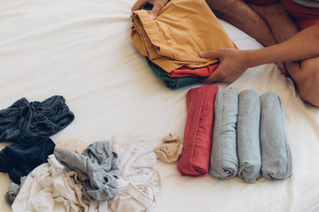 Man is folding and arranging the clothes on the bed.