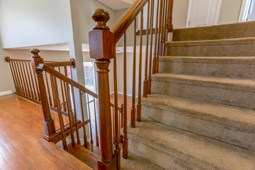 Carpeted staircase with brown handrail inside a house with shiny wooden floor