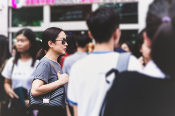 Charming mysterious woman with sunglasses standing outside building in a crowd.