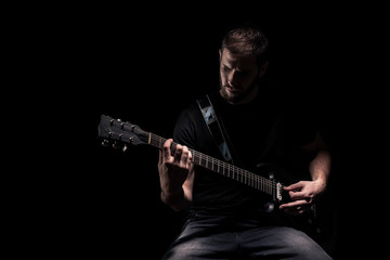 one man, playing guitar, dark and moody rock musician. Shot on black background behind.