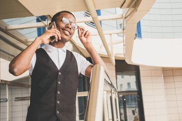 Young african american business man in suit and eyeglasses talking on the phone on the background of the business center