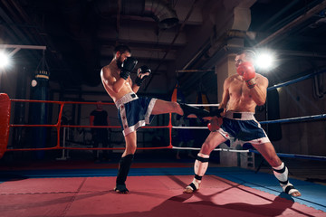 Two angry male kickboxers training kickboxing in the ring at the health club