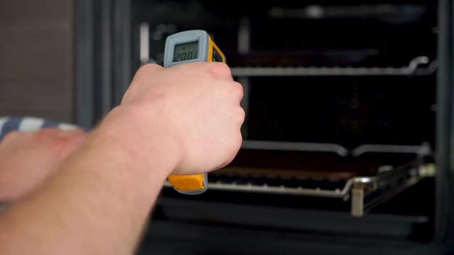Young aspiring chef is checking the temperature of a pizza, bread steel in the oven with a infrared thermometer.