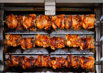 At a stall on a Spanish weekly market, chicken is prepared. They are crispy, fried, and rotate on several skewers on top of each other until they are ready for sale.