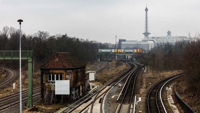 A look in the German capital Berlin on railway tracks and a train station in the district Halensee. In the background are the exhibition halls, the radio tower and a train to be seen in cloudy weather