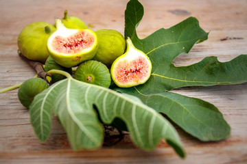 Ripe halved figs on a large fresh green fig leaf on an old raw wood table top
