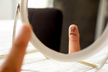 A finger with a sad face looks at himself in the mirror