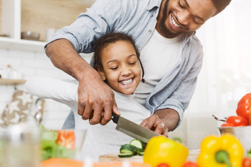 Father teaching his daughter to cut vegetables