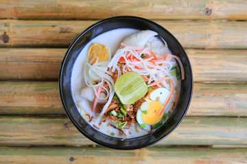 Noodle in coconut milk soup in bowl on bamboo wood table. Fusion Thai food. Top view.