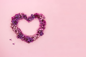 Beautiful lilac flowers in shape of heart on pastel pink background. Top view. Copy space.