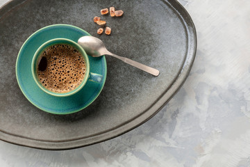 A closeup of a cup of black coffee, shot from the top on a tray with caramelized sugar, a spoon,...