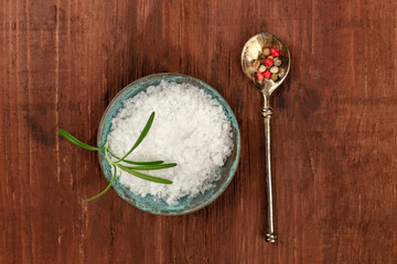 Gourmet spices. Rosemary infused sea salt and a spoon with peppercorns, shot from the top on a dark rustic wooden background with copyspace