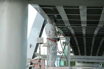 Professional worker in a protective suit and mask paints a bridge from the spray gun  stand on the hydraulic lift.