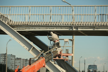 Professional worker in a protective suit and mask paints a bridge from the spray gun  stand on the...