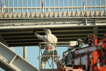 Professional worker in a protective suit and mask paints a bridge from the spray gun  stand on the hydraulic lift.