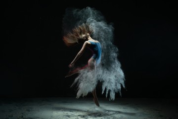 Woman dancing in white dust cloud view in the dark
